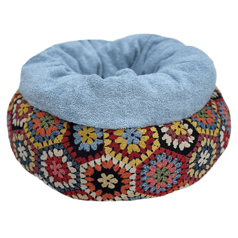 Multicolored crocheted pet bed with a light blue cushion on a transparent background