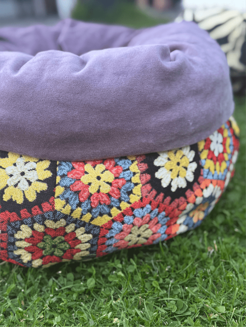 Gray pet bed with a colorful crochet border on grass